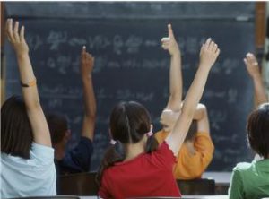 photo of students in a classroom raising their hands